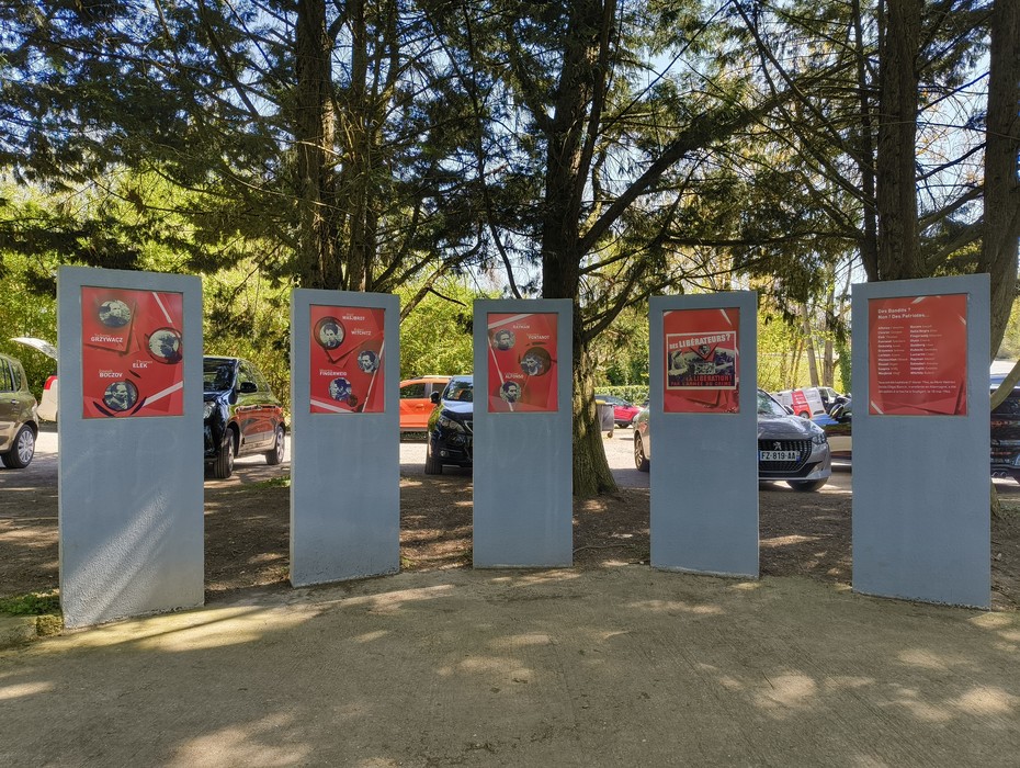Memoriale del Gruppo Manouchian con pannelli informativi e immagini, circondato da alberi e automobili.