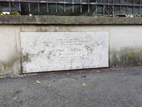 Lapide in memoria di Dino Carta, situata in un'area esterna con alberi e sentieri circostanti.
