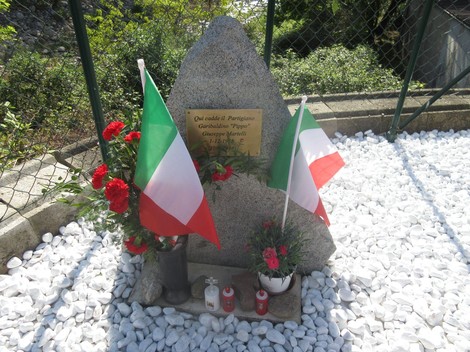 Cippo commemorativo dedicato a Giuseppe Martelli, partigiano, decorato con fiori e bandiere italiane.