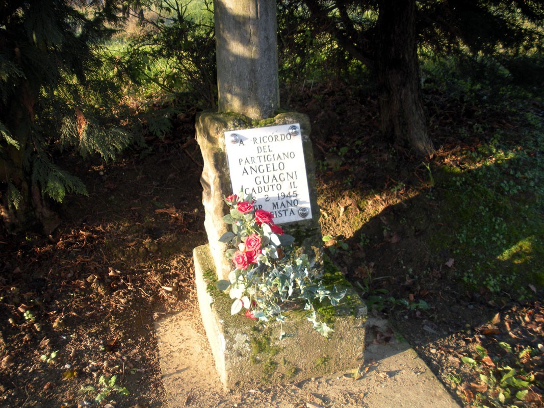 Cippo commemorativo con fiori in ricordo di Angelo Guagni, in un contesto naturale e tranquillo.
