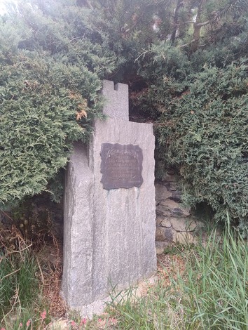 Cippo commemorativo dedicato al contributo delle popolazioni montane, immerso nella vegetazione.