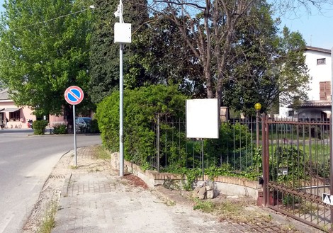Lapide commemorativa in un area verde, visibile da una strada con segnale di divieto di sosta.