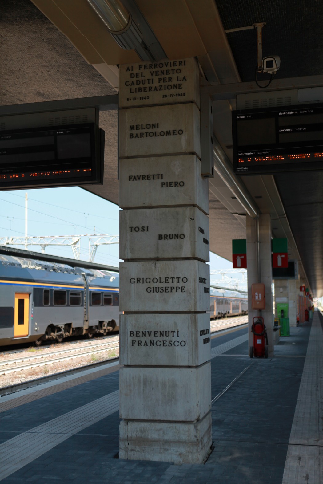 Monumento dedicato ai ferrovieri caduti per la libertà, con nomi incisi su un pilastro in una stazione ferroviaria.