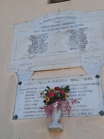 Lapide commemorativa dedicata ai caduti di Ghezzano, decorata con fiori freschi.