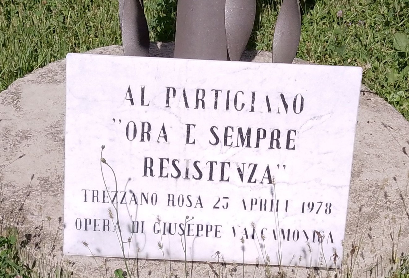 Monumento al partigiano con dedica evocativa e data, immerso in un contesto verde e naturale.