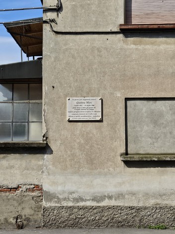 Lapide commemorativa a Mori, posizionata su un edificio con parete in muratura e finestre di vetro.