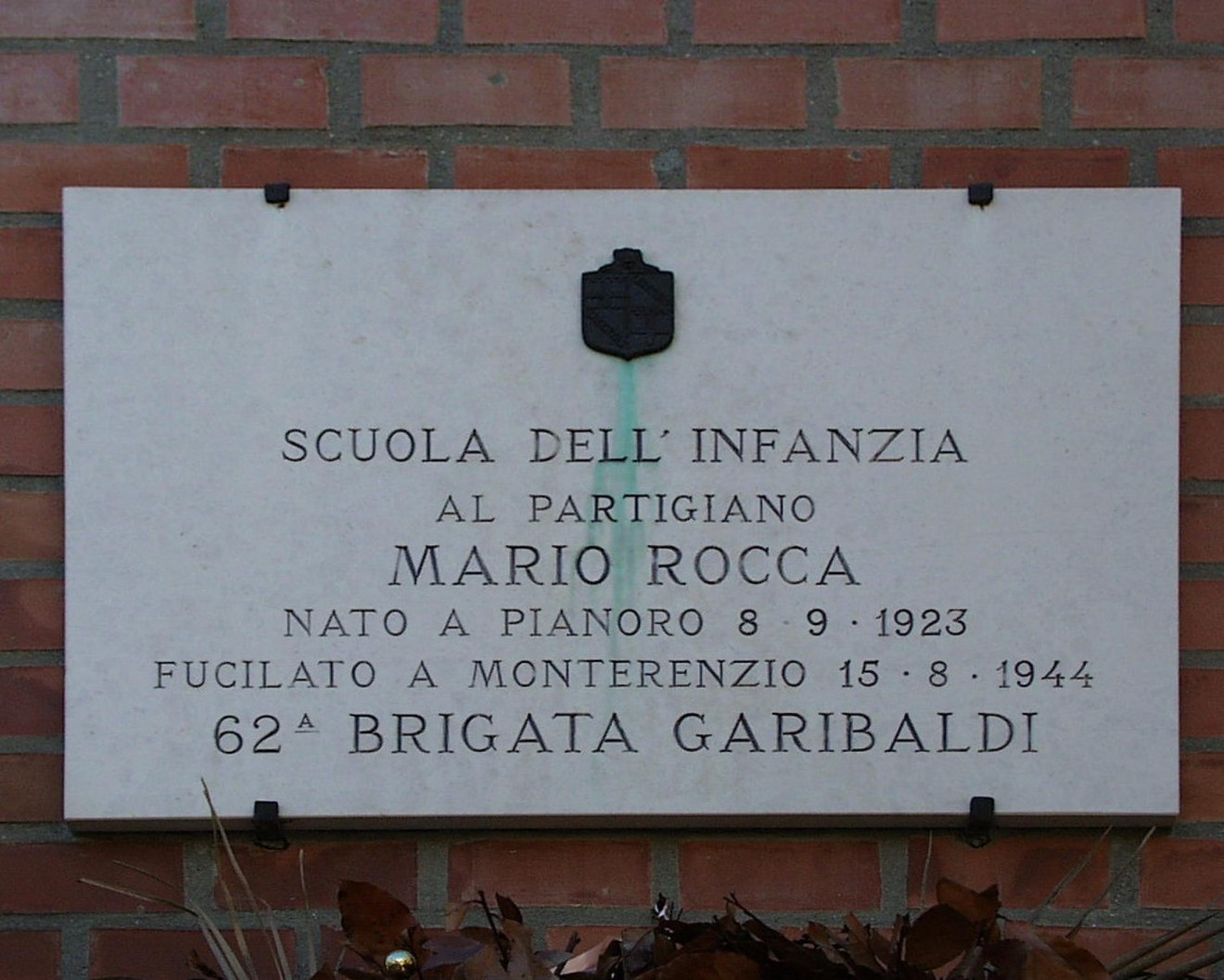 Lapide commemorativa in onore di Mario Rocca, partigiano fucilato nel 1944, situata in una scuola dell'infanzia.