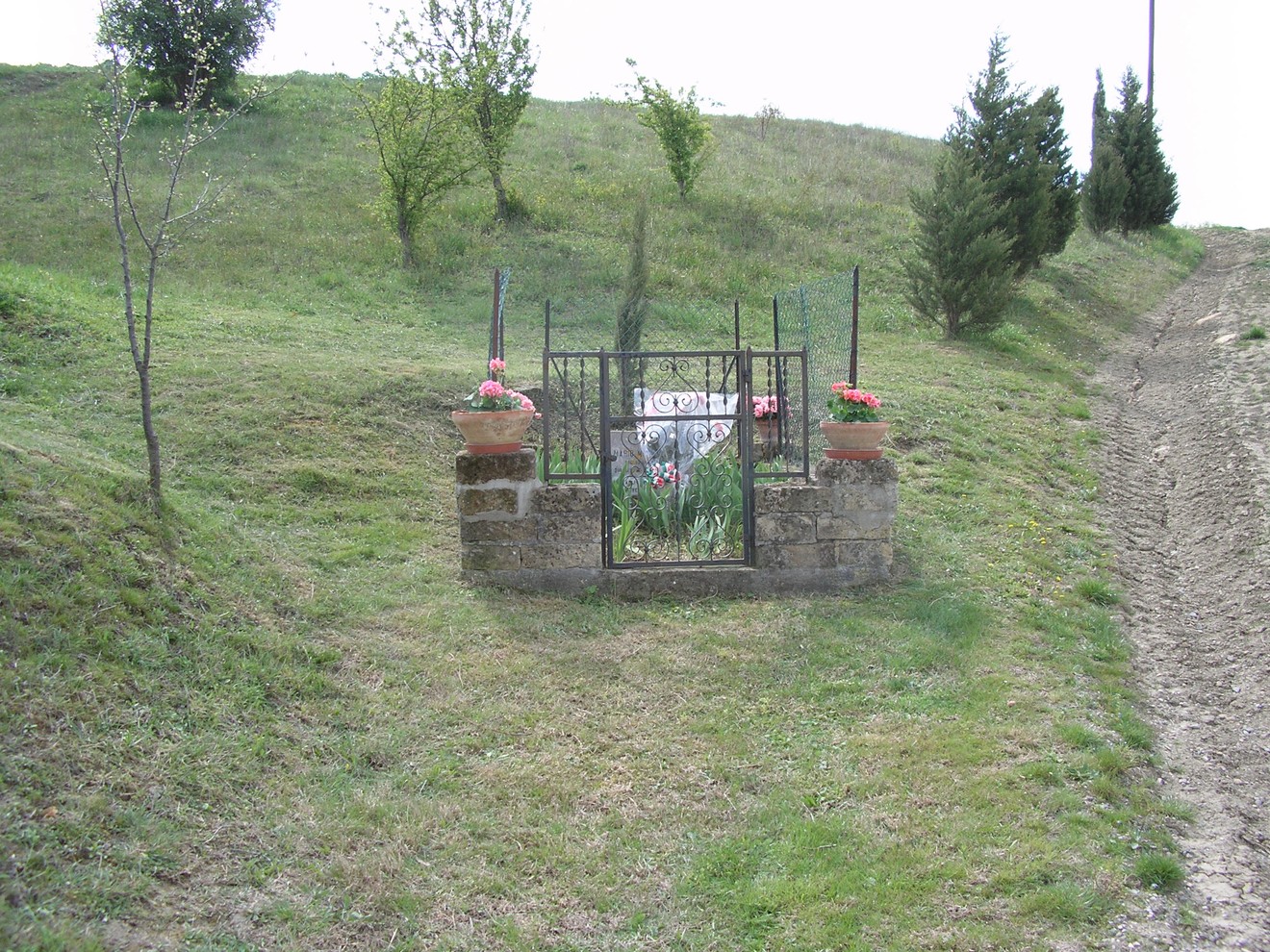 Cippo commemorativo situato in un'area verde, circondato da piante e fiori.