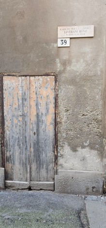 Lapide commemorativa in muratura con porta in legno usurata, situata su un muro di pietra.