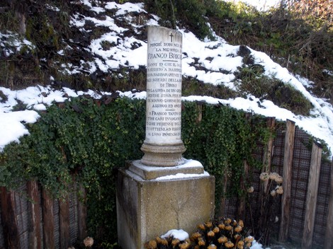 Cippo commemorativo di Franco Brichetti, circondato da neve e vegetazione, situato in un'area rurale.