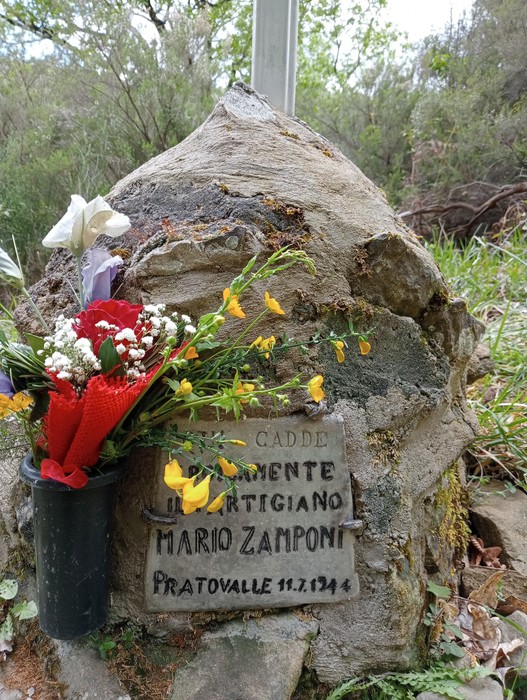 Cippo commemorativo di Mario Zamponi, con fiori e decorazioni, immerso nella natura.