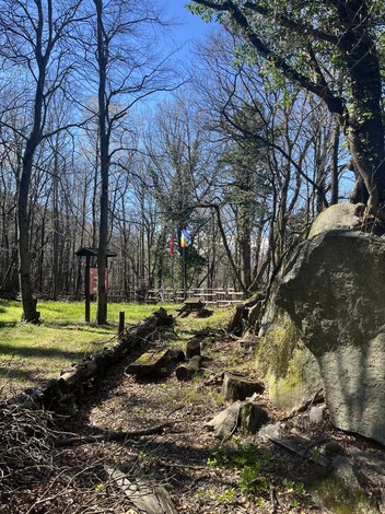 Spazio nel bosco con targhe dedicati a giuramenti, circondato da alberi e bandiere.