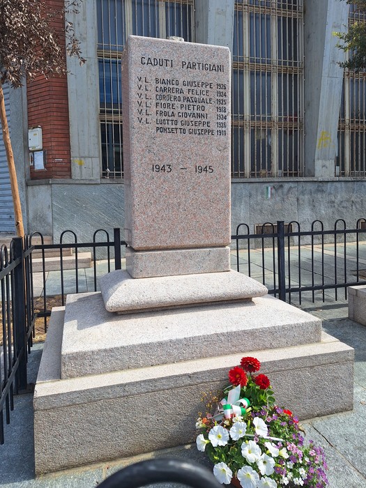 Monumento ai caduti con pietra commemorativa e fiori, situato in un'area pubblica.