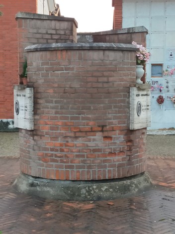 Monumento commemorativo dedicato a Ghirardelli, Ravaioli e Tosi, realizzato in mattoni, con fiori e targhe.