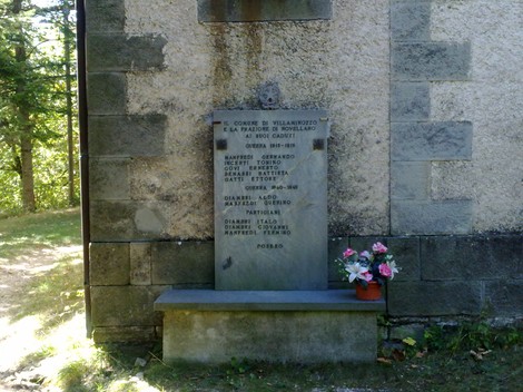 Cippo commemorativo ai Caduti di Novellano, con dedica ai martiri della zona. Fiori adornano la base.