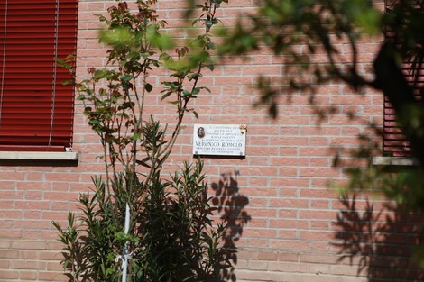 Lapide commemorativa su un muro di mattoni rossi, circondata da piante verdi.