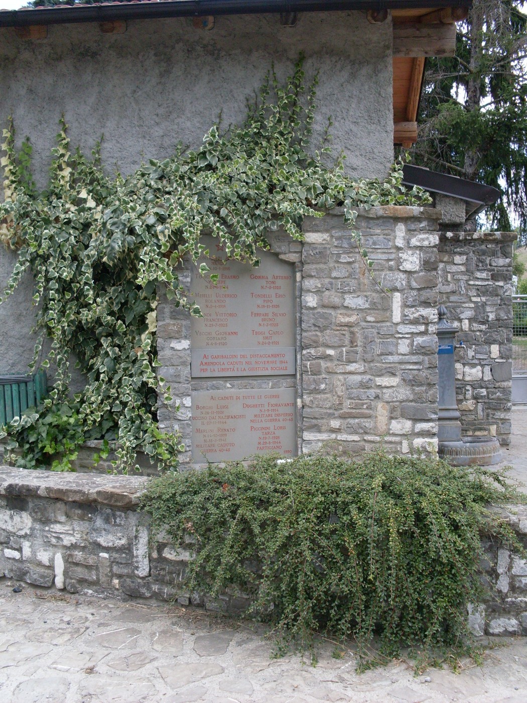 Lapide commemorativa in onore dei caduti del Distaccamento Amendola, decorata da vegetazione.