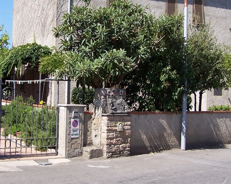 Cippo commemorativo a Caprai e Creatini, circondato da vegetazione e recinzione.