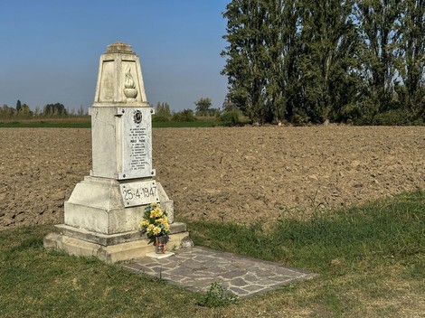Monumento a Marri, commemorazione con fiori e dedica in un campo aperto, sullo sfondo un cielo blu.