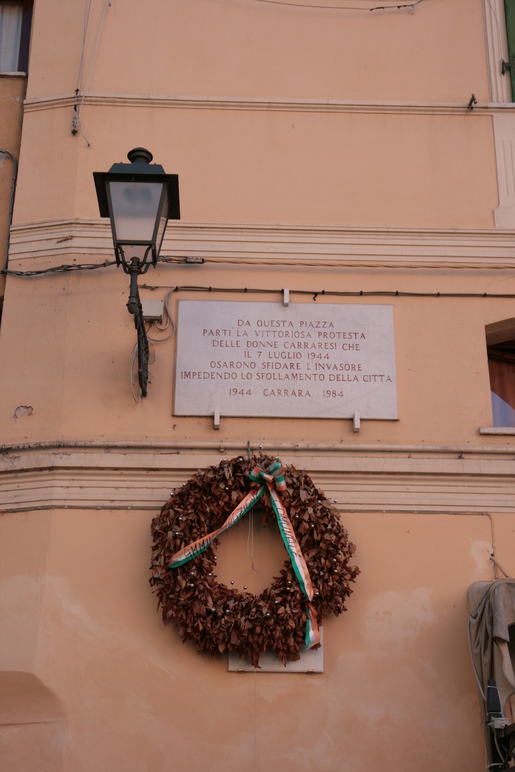 Lapide commemorativa dedicata alla rivolta delle donne, con corona di foglie, ubicata in piazza a Carrara.