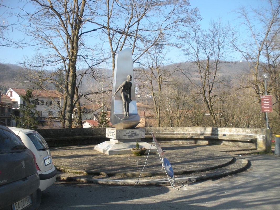 Monumento ad Anselmi in un'area verde, con statue e alberi sullo sfondo, rappresenta un tributo alla memoria.