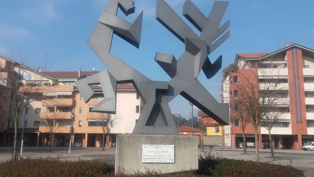 Monumento a Pertini, un'opera moderna in metallo, situata in una piazza circondata da edifici residenziali.