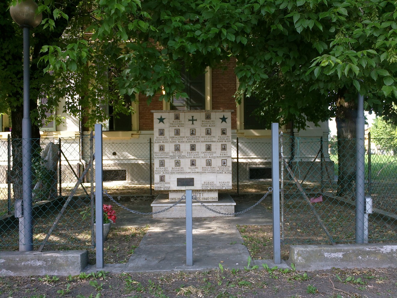 Monumento commemorativo ai Caduti di Castellazzo, immerso nel verde e recintato da una rete.