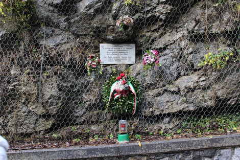 Lapide commemorativa adornata da fiori su una parete rocciosa in un contesto naturale.
