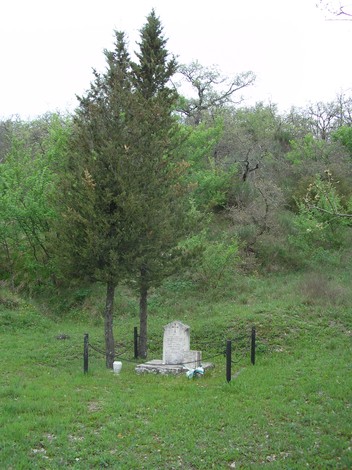 Cippo in un'area verde, circondato da alberi, a commemorazione di Tassi e Magi. Ambiente naturale e tranquillo.