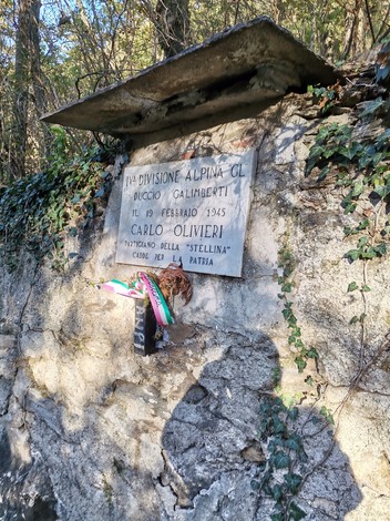 Lapide commemorativa dedicata a Carlo Olivieri, affissa su una parete rocciosa in un contesto naturale.