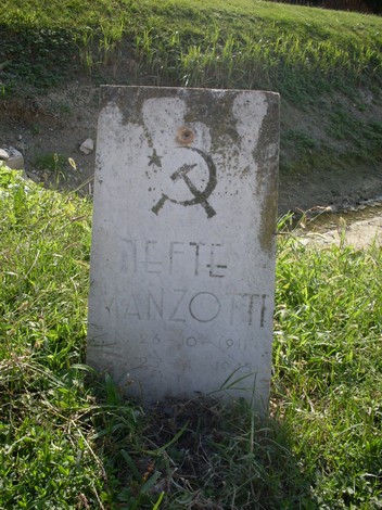 Cippo commemorativo di Manzotti, con simboli e iscrizioni, immerso nel verde della campagna.