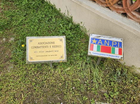 Largo Martiri del Nazifascismo, con targa commemorativa e simboli dell'ANPI. Spazio verde e ambiente urbano.