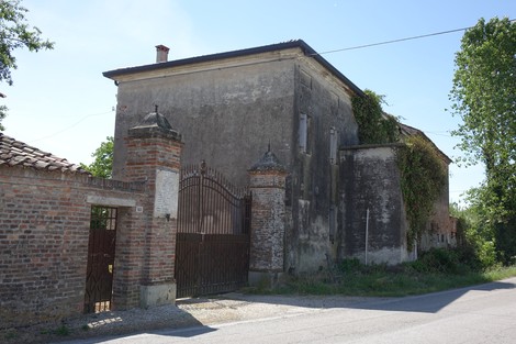 Lapide della fattoria Bogoni, mostra l'ingresso di un edificio rurale con mura degradate e cancello metallico.
