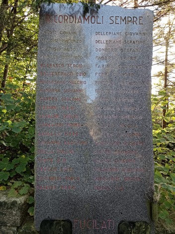 Memoriale dedicato ai caduti della Benedicta, con nomi incisi su una stele di pietra, circondato dalla natura.