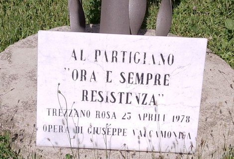 Monumento al partigiano con dedica evocativa e data, immerso in un contesto verde e naturale.