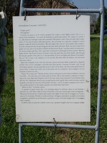 Cippo commemorativo a Cocconi, con scritte su un supporto metallico, immerso in un'area verde.