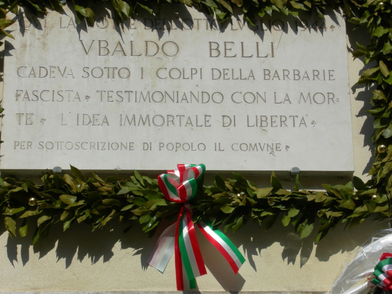 Lapide commemorativa di Vivaldo Belli, dedicata alla memoria e libertà, ornata con un festone di alloro.