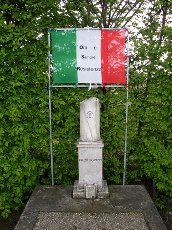 Cippo a Piron, monumento dedicato alla resistenza, con bandiera tricolore italiana sullo sfondo.