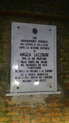 Lapide in marmo con iscrizione, fissata su una parete di mattoni a vista.