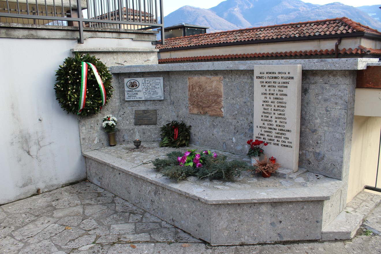 Monumento commemorativo con dettagli in pietra e fiori freschi, dedicato ai fratelli Pellegrini.