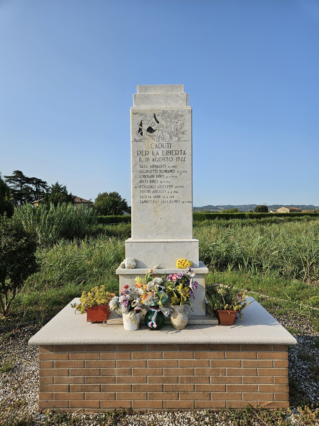 Monumento ai Martiri di Ponte Ruffio con fiori e un paesaggio verde sullo sfondo.