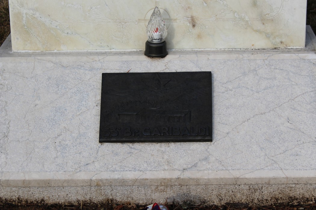 Lapide commemorativa dedicata ai caduti, con un oggetto luminoso nella parte superiore.