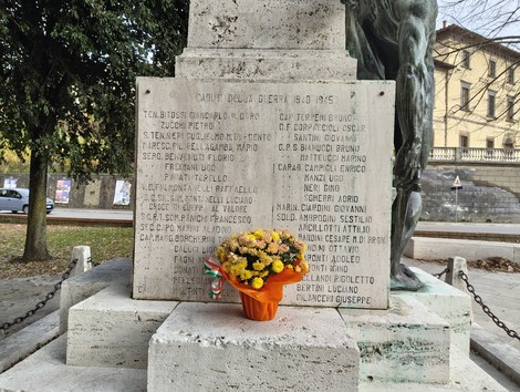 Monumento ai caduti con fiori freschi davanti e nomi incisi su una stele commemorativa.