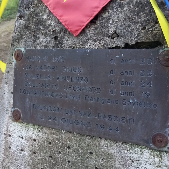 Cippo commemorativo con nomi di partigiani uccisi dai nazifascisti nel 1944. Bandiera e decorazioni presenti.
