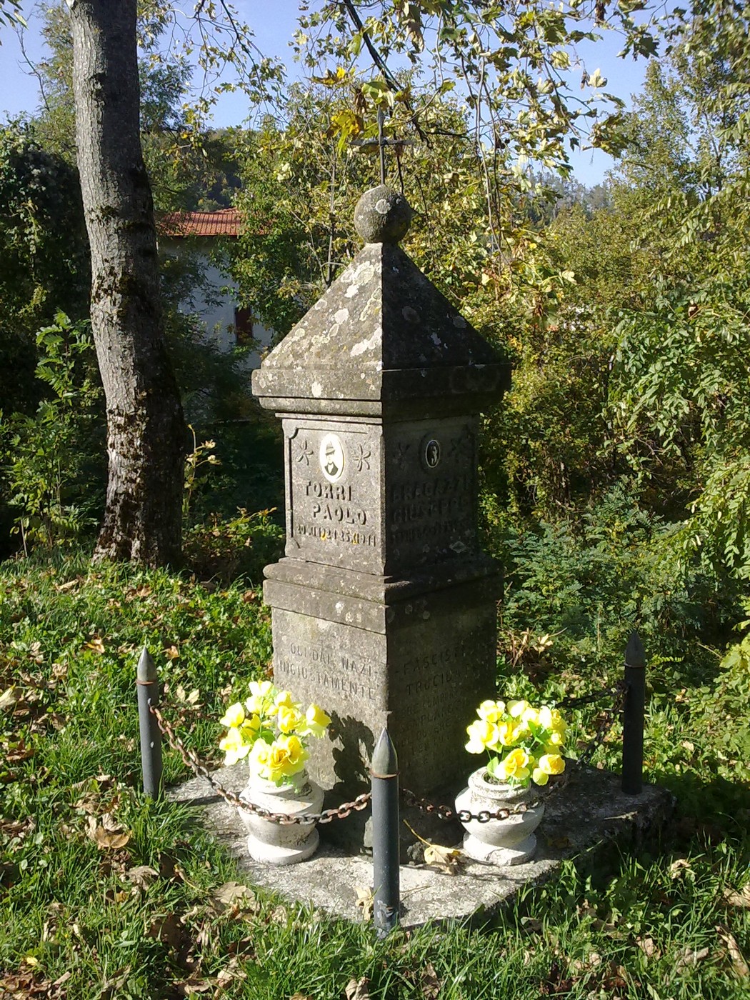 Cippo in pietra circondato da fiori, immerso nel verde, rappresenta un memoriale a Torri e Bragazzi.