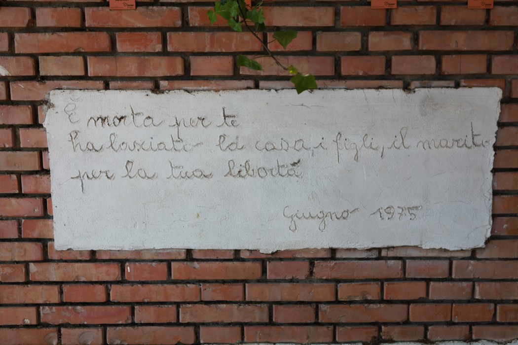 Monumento dedicato alle 128 partigiane, con scritta commemorativa su muro di mattoni.