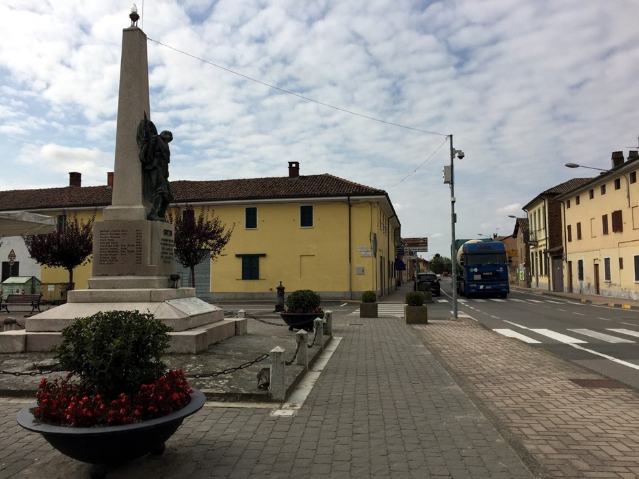 Monumento ai Caduti di Cozzo, situato in una piazza con edifici storici e vegetazione.