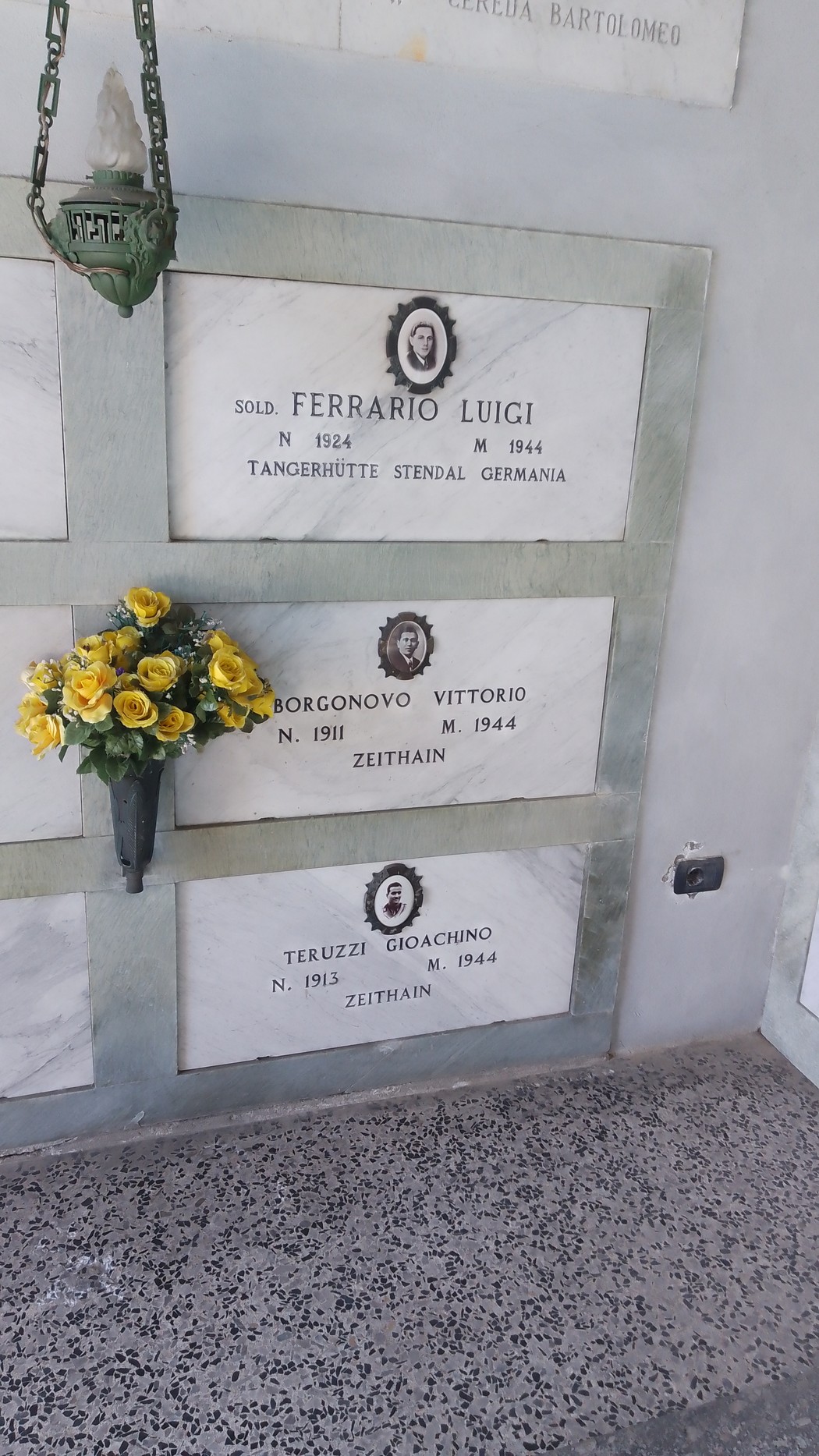 Cappella ai caduti di Brugherio con lapidi commemorative e un mazzo di fiori gialli.