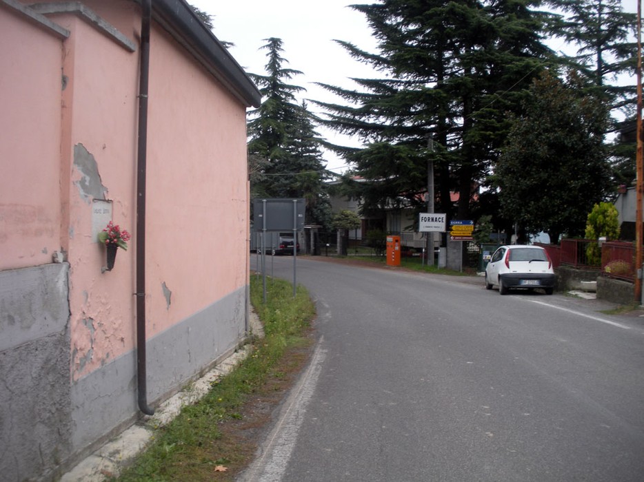 Vista di una via con un edificio rosa e vegetazione, che conduce a un'area abitativa.