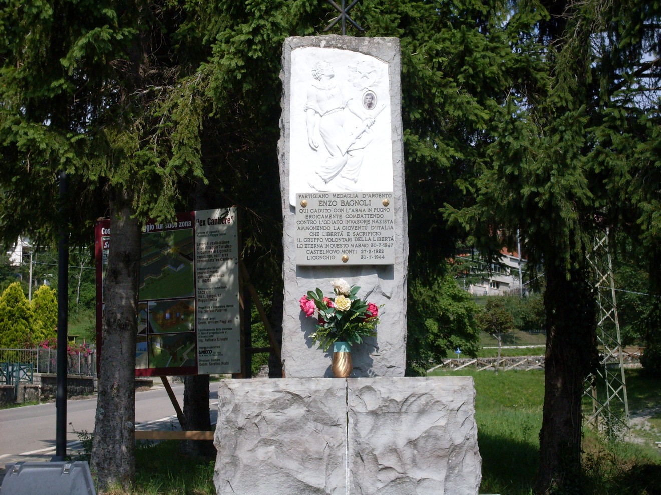 Monumento a Bagnoli dedicato a Enzo Biacchi, con fiori e incisioni commemorative, immerso nel verde.